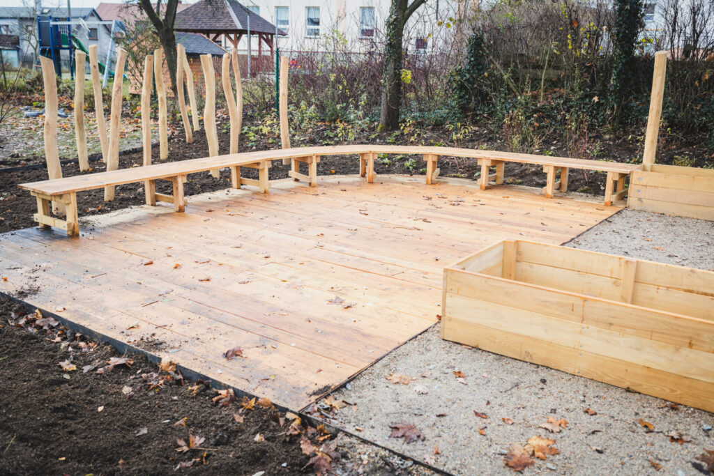 Oblouková dřevěná lavice a terasa z akátového dřeva sloužící jako venkovní učebna.